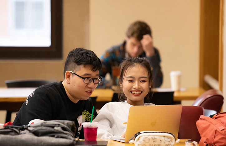 Two Asian students studying together on a laptop computer in the library